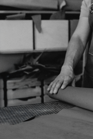 Man rolls out leather. Every pair of 1812 shoes begins not in a factory, but in a workshop.