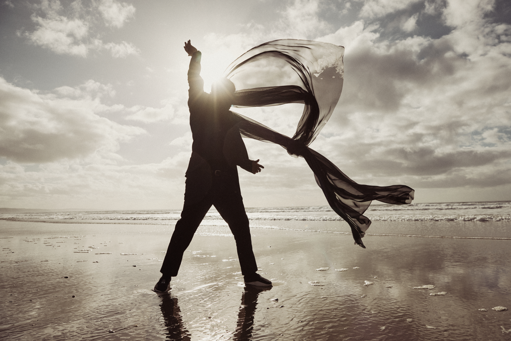 A Masked Journey Through History a man on a beach in golden sunlight whos face in shaddow is hidden by a long flowing black scarf