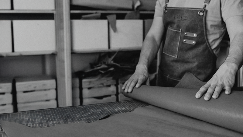 Man rolls out leather. Every pair of 1812 shoes begins not in a factory, but in a workshop.