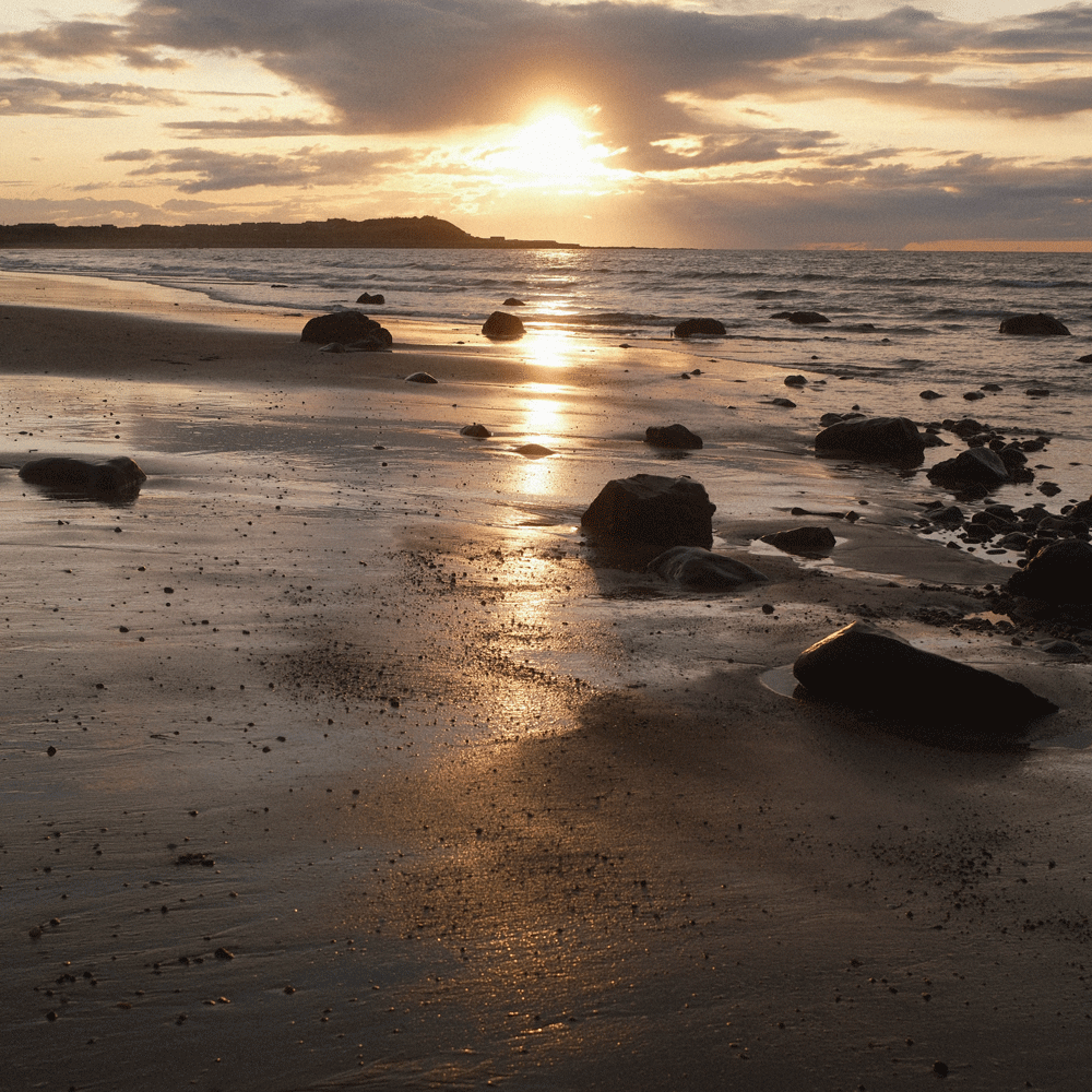 Sunset over a beach with rocks and water reflections